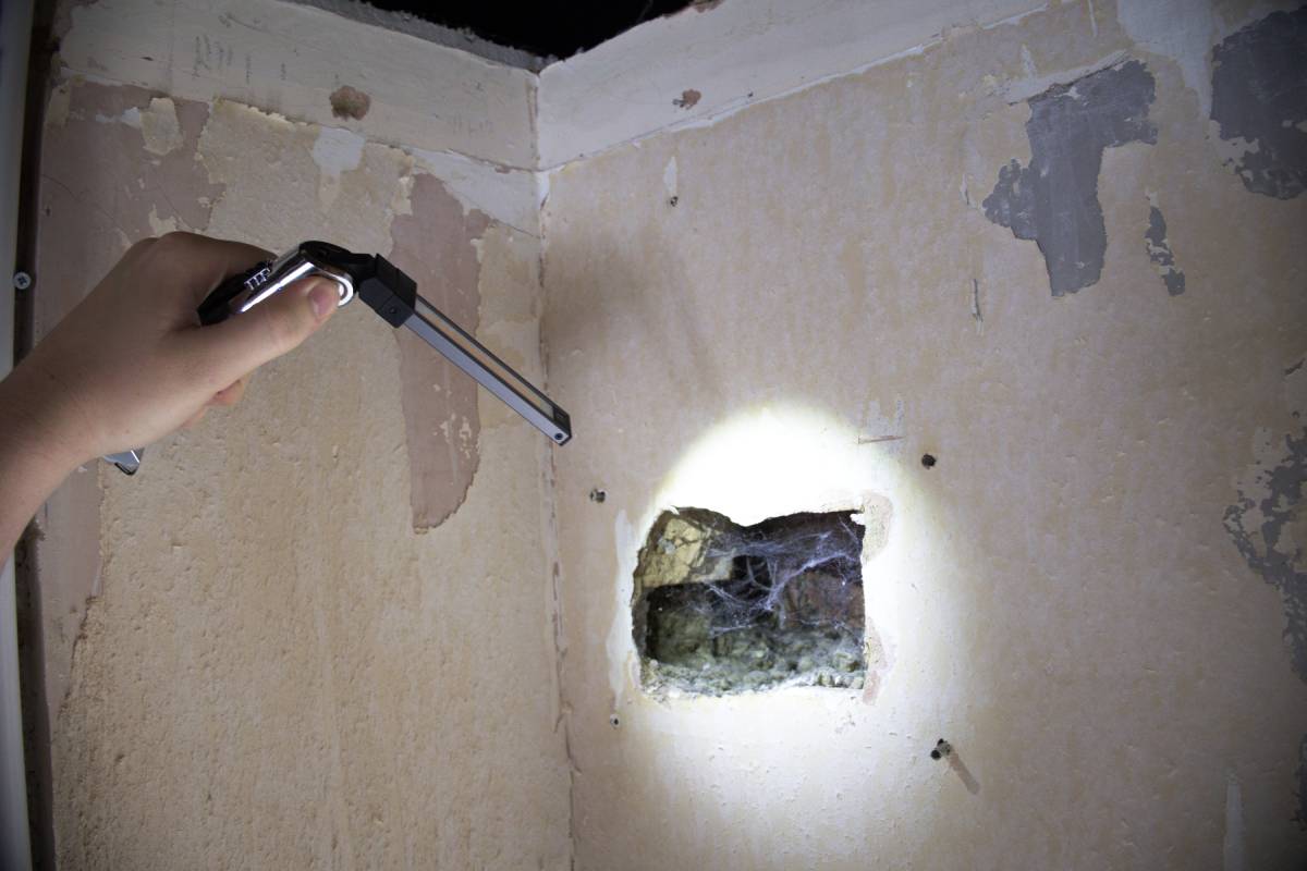 Person using a flashlight to inspect a hole in a wall